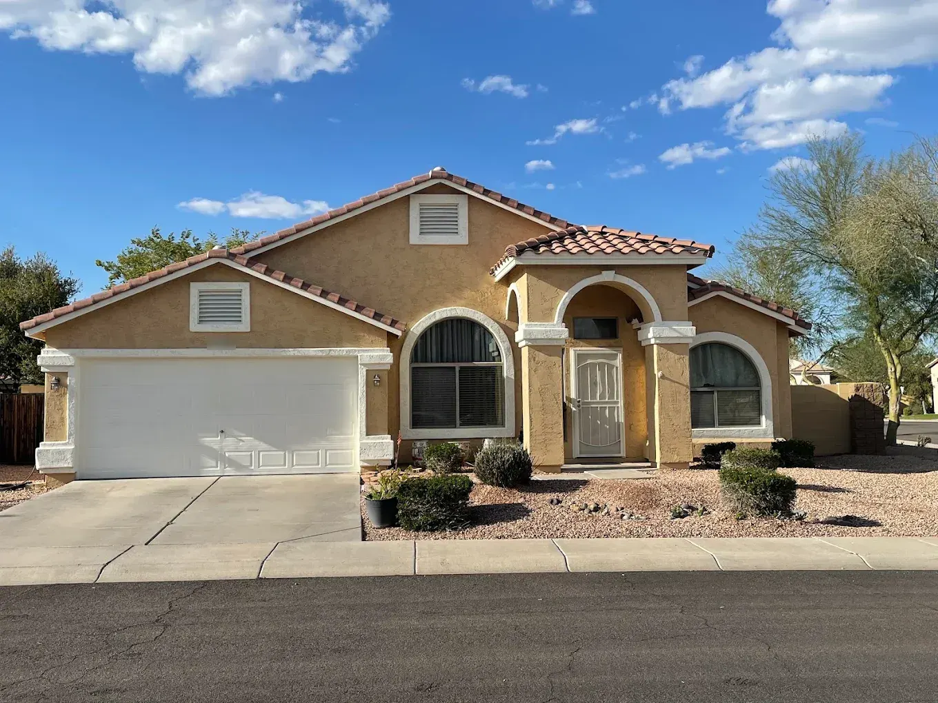 Freshly painted tan stucco home with crisp white trim around arched windows under a blue sky