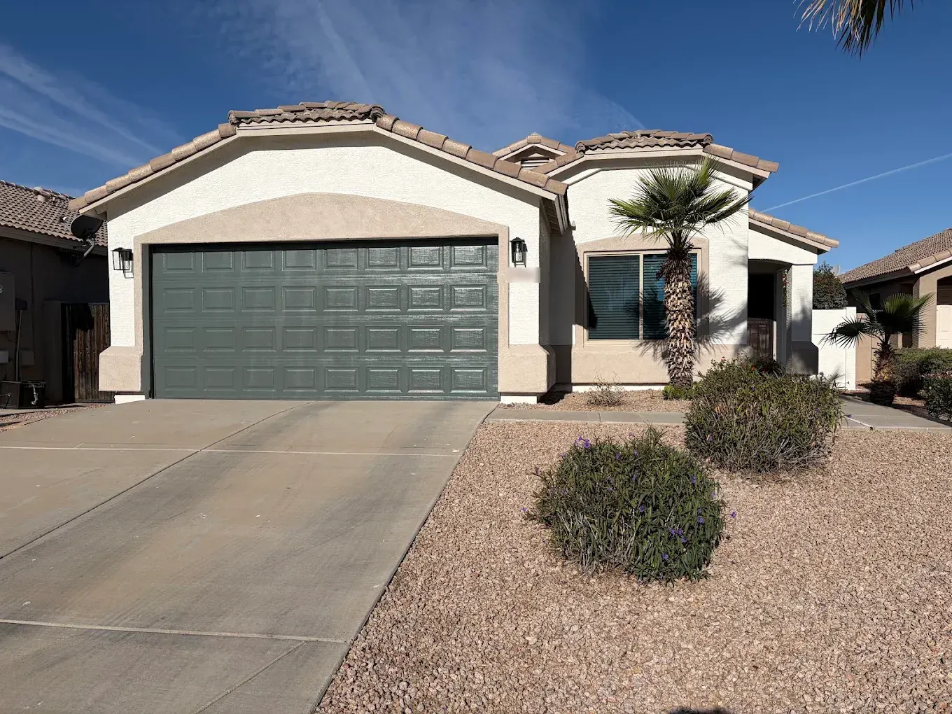 Light stucco home with a deep green garage door and fresh trim