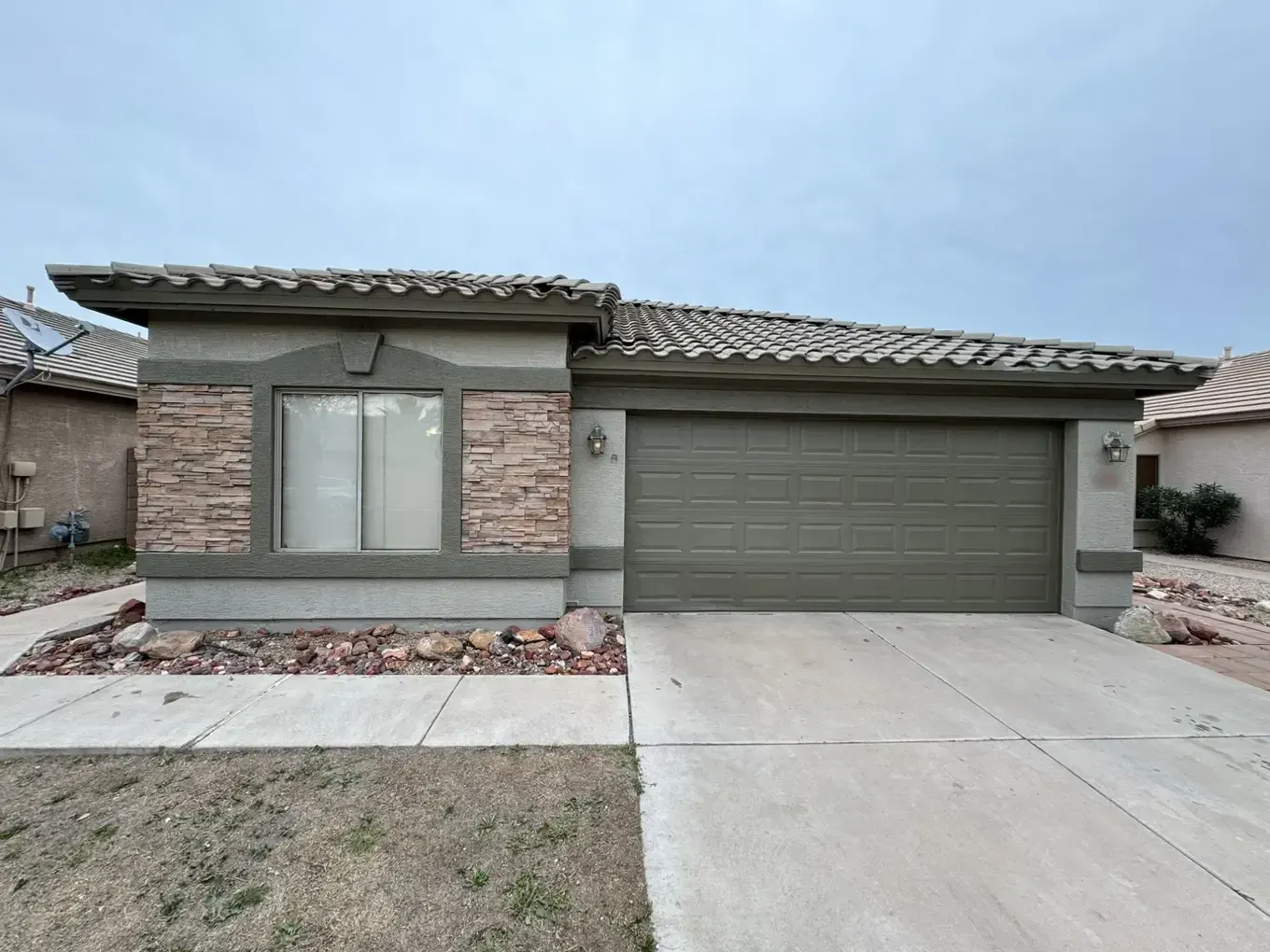 Single-story home painted olive green with a matching garage door beside stone veneer