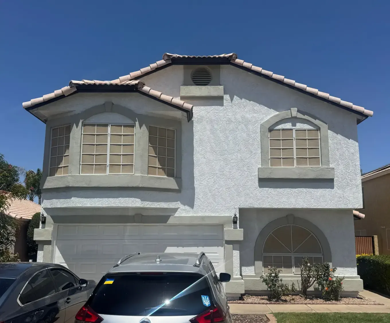 Two-story white stucco home with sage green trim around arched windows