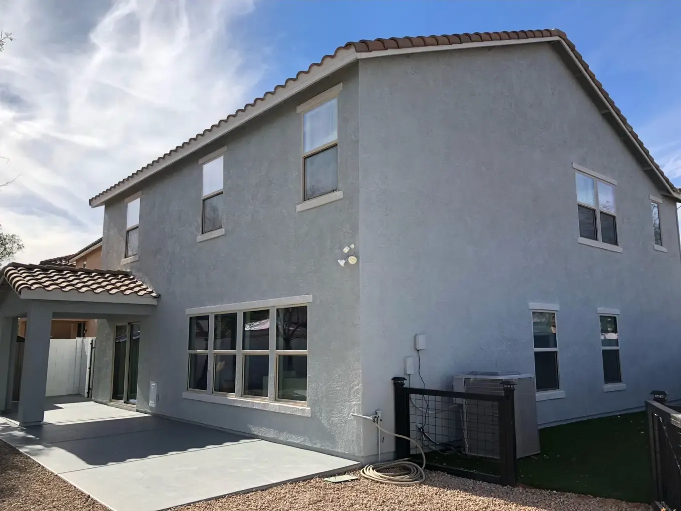 Back of a two-story home with freshly painted gray stucco and light window trim